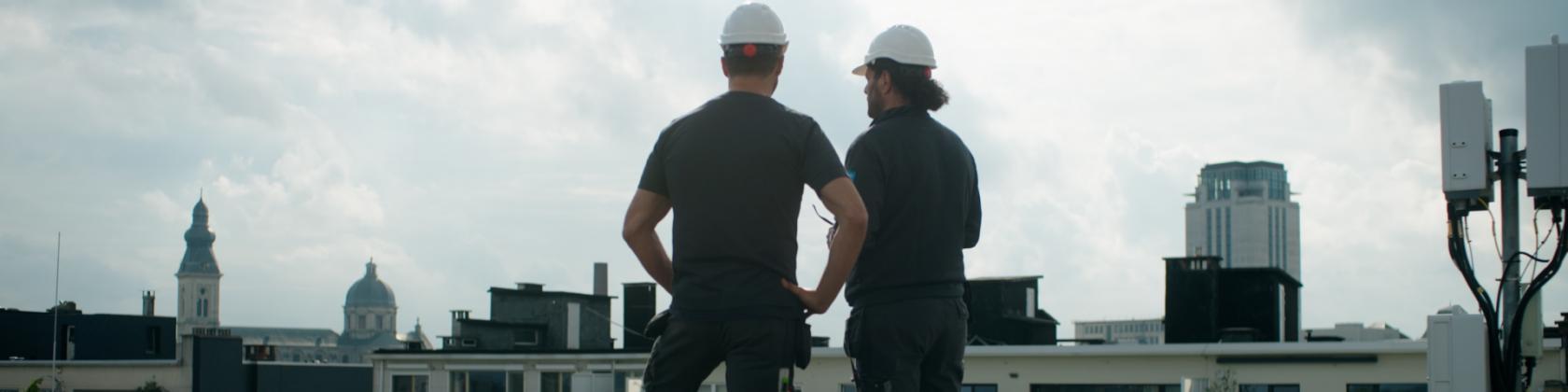 Twee HVAC techniekers die op het dak staan met de skyline van Gent op de achtergrond